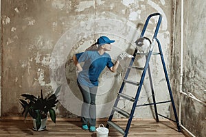 A young woman in a blue t-shirt and a baseball cap makes repairs in the apartment.