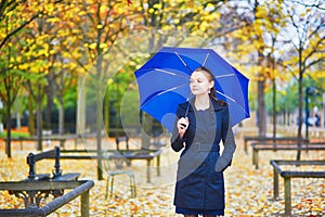 Young woman with blue umbrella in the Luxembourg garden of Paris on a fall or spring rainy day