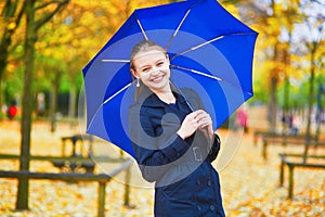 Young woman with blue umbrella in the Luxembourg garden of Paris on a fall or spring rainy day