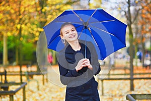 Young woman with blue umbrella in the Luxembourg garden of Paris on a fall or spring rainy day