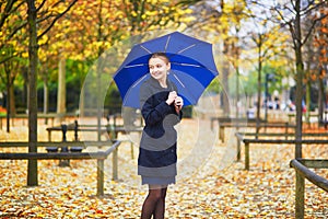 Young woman with blue umbrella in the Luxembourg garden of Paris on a fall or spring rainy day