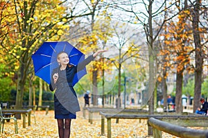 Young woman with blue umbrella in the Luxembourg garden of Paris on a fall or spring rainy day