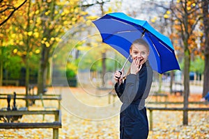 Young woman with blue umbrella in the Luxembourg garden of Paris on a fall or spring rainy day