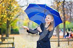 Young woman with blue umbrella in the Luxembourg garden of Paris on a fall or spring rainy day