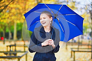 Young woman with blue umbrella in the Luxembourg garden of Paris on a fall or spring rainy day