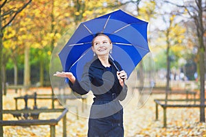 Young woman with blue umbrella in the Luxembourg garden of Paris on a fall or spring rainy day