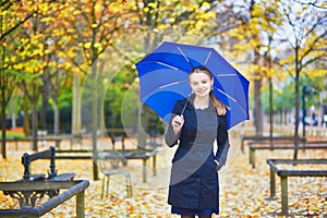 Young woman with blue umbrella in the Luxembourg garden of Paris on a fall or spring rainy day