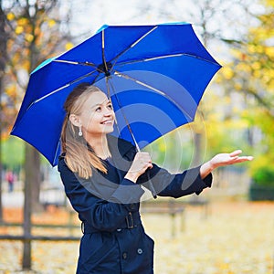 Young woman with blue umbrella in the Luxembourg garden of Paris on a fall or spring rainy day