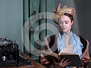 Young woman in blue vintage dress late 19th century reading the book in retro room