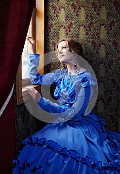 Young woman in blue vintage dress looking out the window in coup