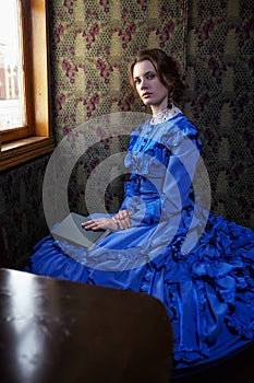 Young woman in blue vintage dress sitting with book in coupe of