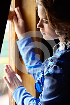 Young woman in blue vintage dress standing near window in coupe