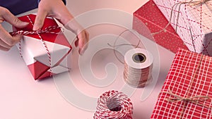 A young woman in blue is wrapping, packaging beautiful gift box for holiday with wrapper and rope to tie a bow-knot, lifestyle, cl