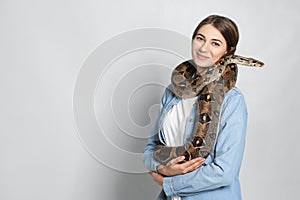 Young woman with boa constrictor on background, space for text. Exotic pet