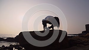 Young woman in bodysuit practicing yoga on the beach above sea at amazing sunrise. Fitness, sport, yoga and healthy