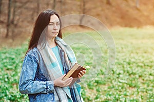 Young woman with book on the walk. Time for reading. Reading book concept. Woman enjoying spring day at nature