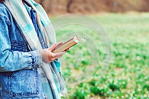 Young woman with book on the walk. Time for reading. Reading book concept. Woman enjoying spring day at nature