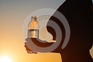 Young woman with bottle water after jogging on the sunset backgrounds. Top view on the city