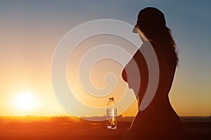 Young woman with bottle water after jogging on the sunset backgrounds. Top view on the city