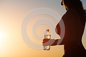 Young woman with bottle water after jogging on the sunset backgrounds. Top view on the city