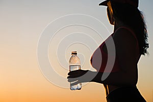 Young woman with bottle water after jogging on the sunset backgrounds. Top view on the city