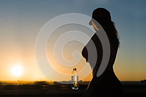 Young woman with bottle water after jogging on the sunset backgrounds. Top view on the city