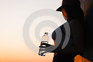 Young woman with bottle water after jogging on the sunset backgrounds. Top view on the city