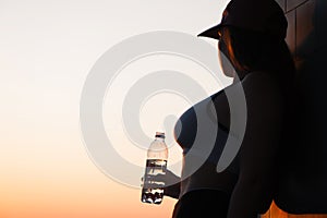 Young woman with bottle water after jogging on the sunset backgrounds. Top view on the city