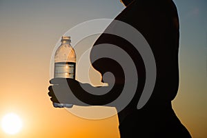 Young woman with bottle water after jogging on the sunset backgrounds. Top view on the city