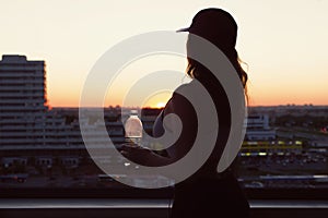 Young woman with bottle water after jogging on the sunset backgrounds. Top view on the city