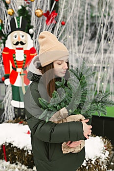 Young woman with a bouquet of Christmas tree branches in a craft package in her hands in winter near the cafe's