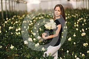 Young woman with bouquet of white roses stand inside roses plantation in greenhouse