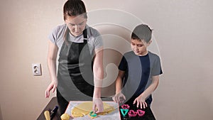 Young woman and boy cut different shapes from dough