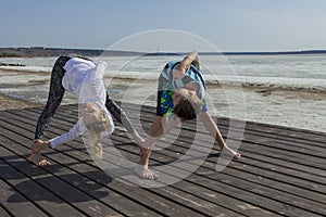 Young woman and boy doing wide legged Forward Bend, twist variation.