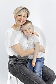 A young woman and a boy are hugging and smiling. Mom holds her 4-year-old son on her lap. Love and tenderness. White background.