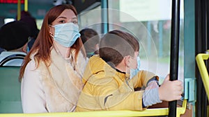 Young woman and boy take precautions in public place and wear medical mask while traveling in city bus