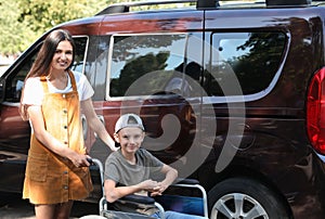Young woman with boy in wheelchair near van
