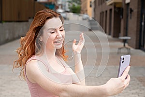 Young woman with braces on her teeth smiles and takes a selfie on a smartphone outdoors.