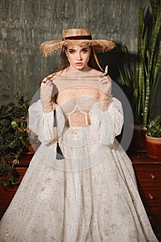 A young woman with bridal makeup in a fashionable wedding dress and straw hat. Beautiful model girl wearing a stylish