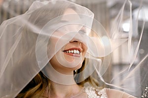 A young woman bride in a wedding dress rejoices and covers her face with a vei