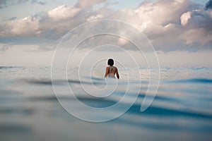 Young woman in bright bikini surfing on a board in ocean