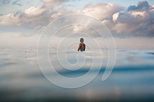 Young woman in bright bikini surfing on a board in ocean