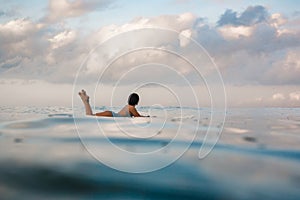 Young woman in bright bikini surfing on a board in ocean