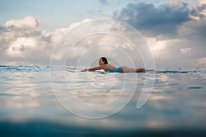 Young woman in bright bikini surfing on a board in ocean