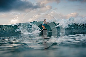 Young woman in bright bikini surfing on a board in ocean