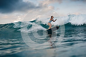 Young woman in bright bikini surfing on a board in ocean