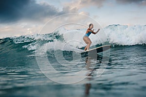 Young woman in bright bikini surfing on a board in ocean