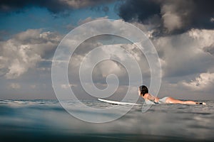 Young woman in bright bikini surfing on a board in ocean