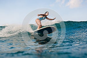 Young woman in bright bikini surfing on a board in ocean