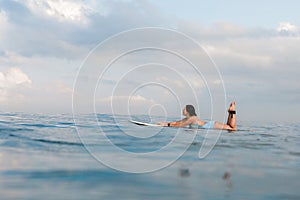 Young woman in bright bikini surfing on a board in ocean